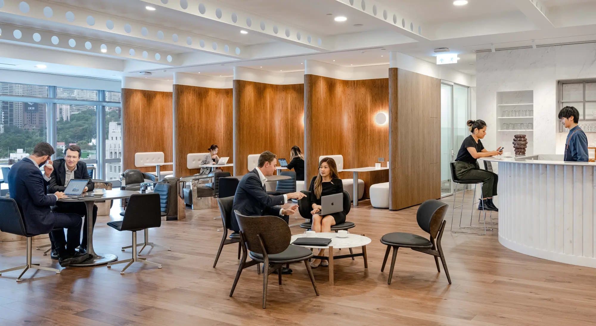 A modern business lounge with curved wood partitions, leather chairs, and city views
