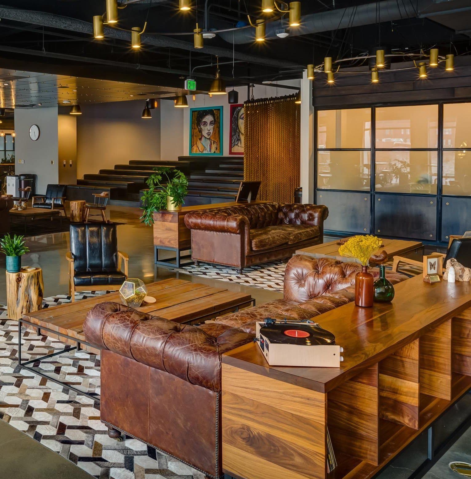 A warmly lit communal lounge with leather chesterfield sofas, wood floors, and brass pendant lights